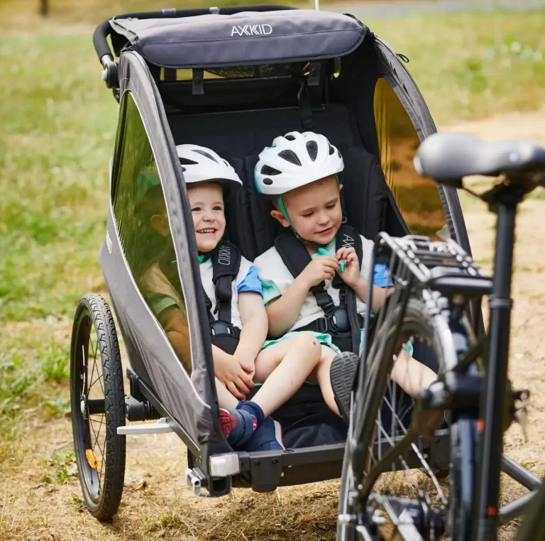 Två barn som sitter i cykelvagnen Axkid Grand Tour. De ser glada ut och verkar nöjda med denna modellen.